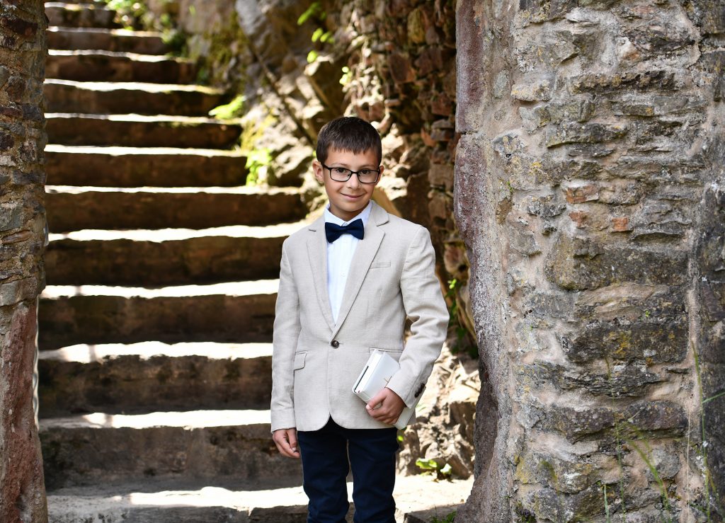 Kommunionshooting in Wadern - Junge lehnt an einer alten Mauer in natürlicher Umgebung