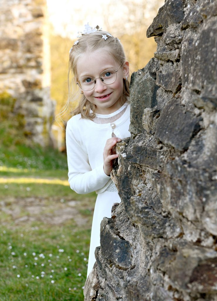 Kommunionmädchen in weißem Kleid an einer Mauer - natürliche Kommunionfotos draußen