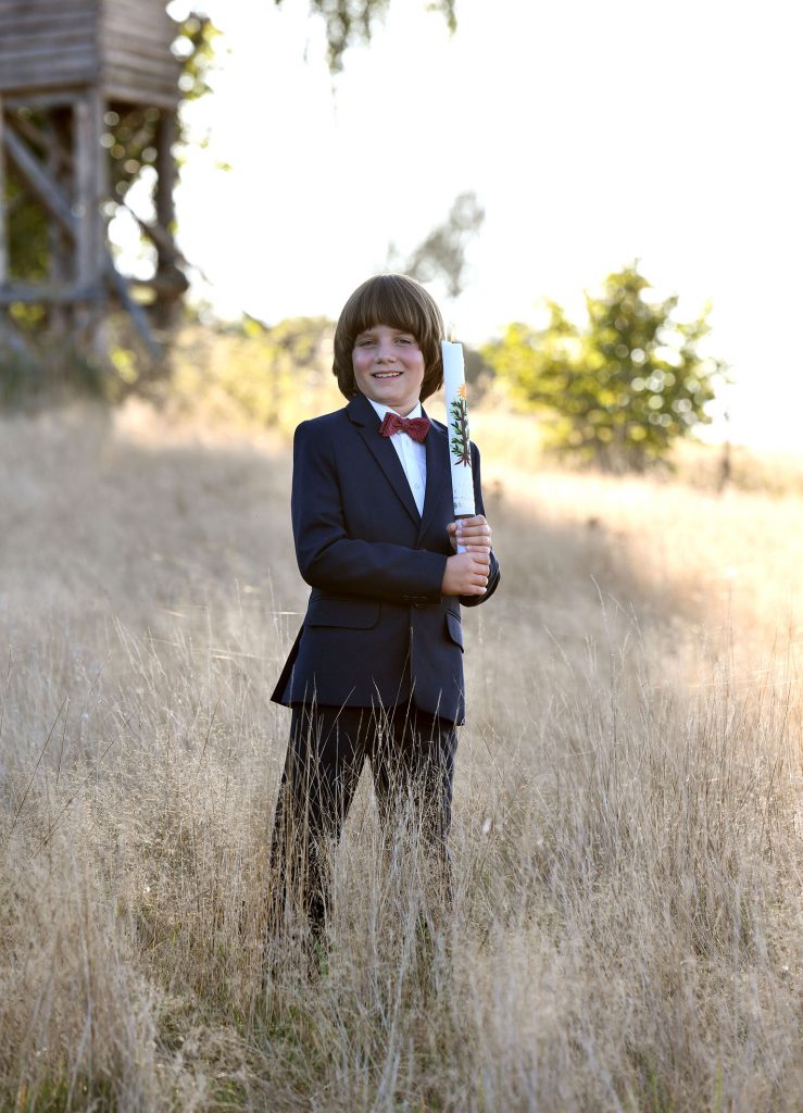Natürliche Kommunionfotos - Junge lächend im hohen Gras mit der Kommunionkerze in der Hand
