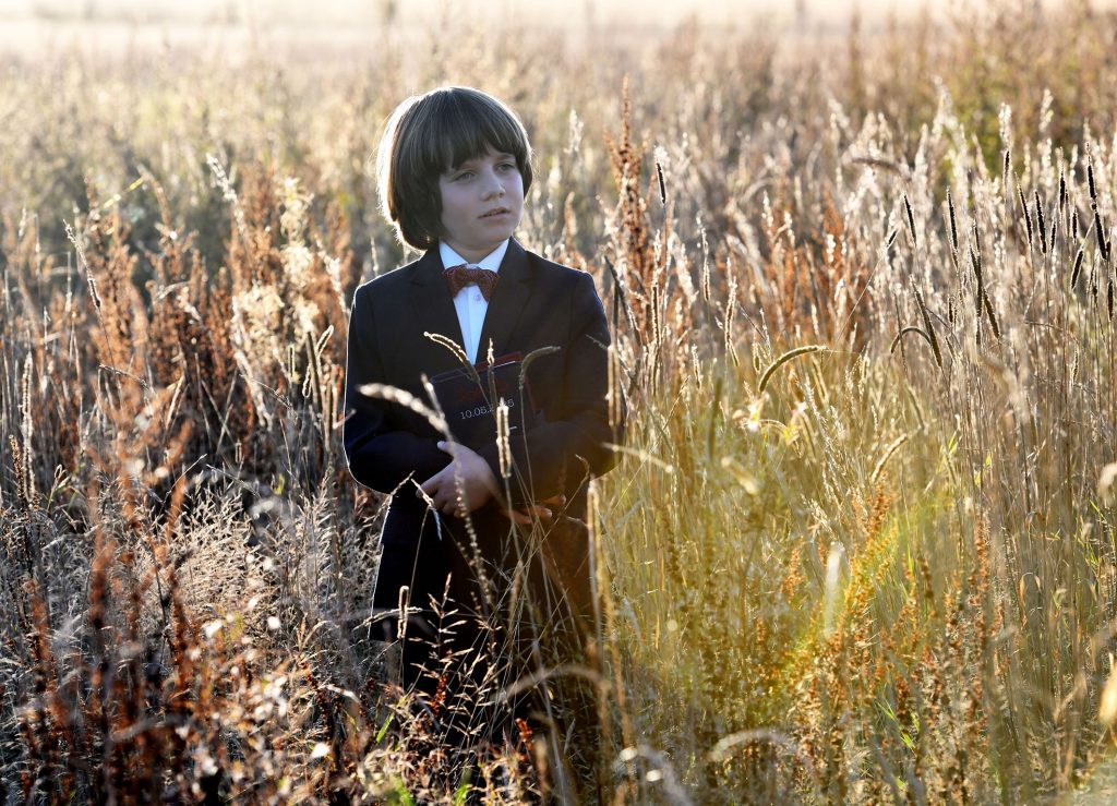 Natürliche Kommunionfotos - Junge im dunklen Anzug mit Gebetbuch im Arm