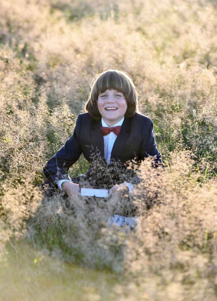 Natrülche Kommunionfotos - lachendes Kommunionkind sitzend in hoher Wiese