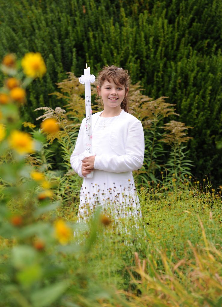 Kommunionmädchen in weißem Kleid mit Kerze
