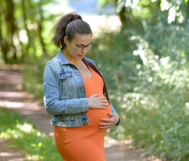 Mom to be in orangenem Kleid und Jeansjacke draußen