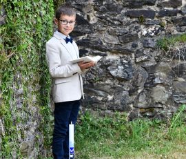 Kommunionkind im Anzug und Kerze in der Natur