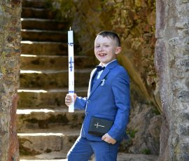 Kommunionkind im Anzug und Kerze in der Natur