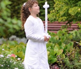 Kommunionfoto eines Mädchens mit Kerze im Grünen